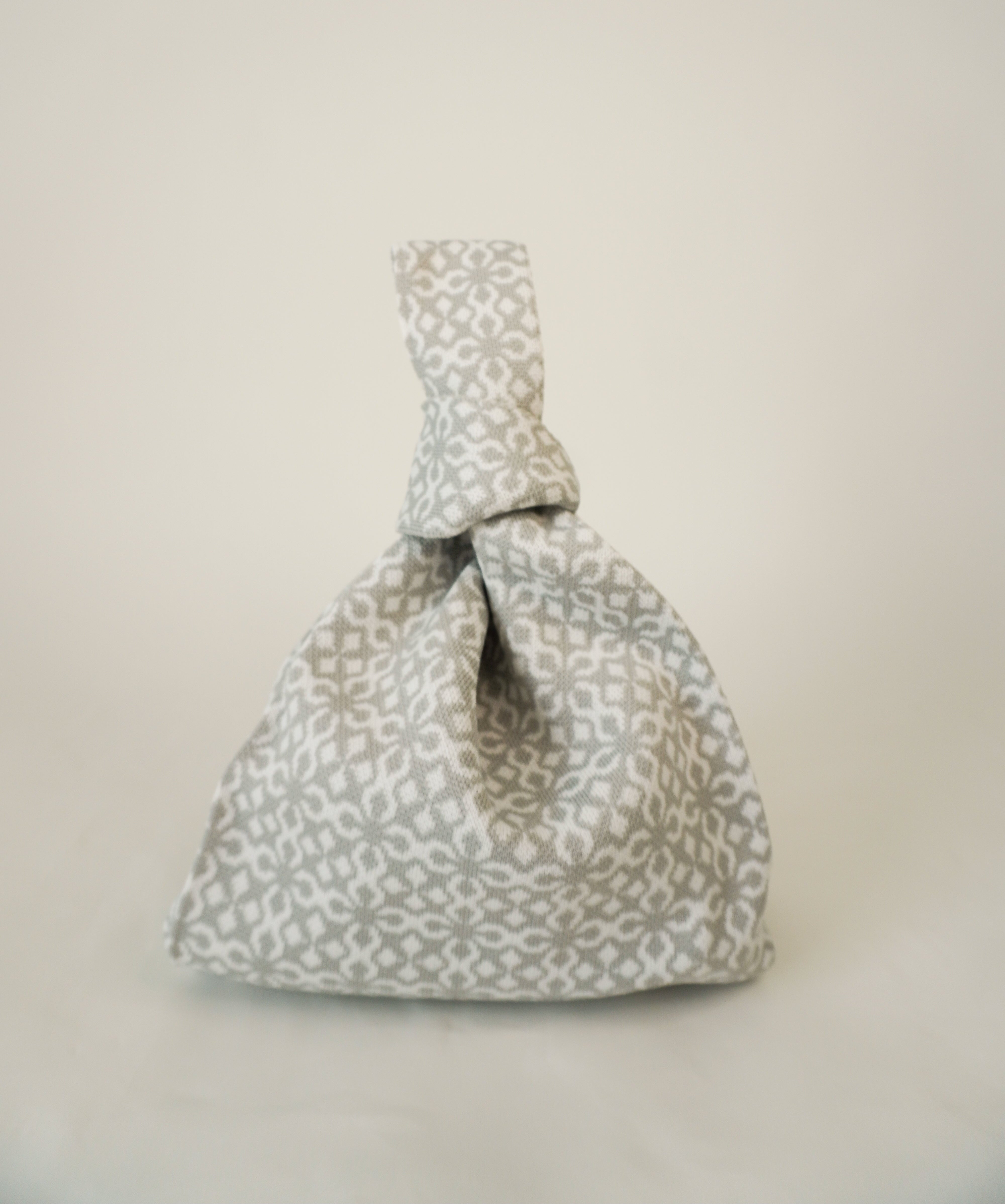 Grey drawstring handbag with all-over floral geometric pattern and gathered top.