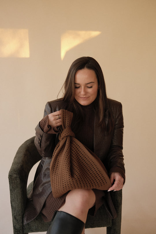 Brown crochet drawstring handbag held by a person; perforated knit texture visible