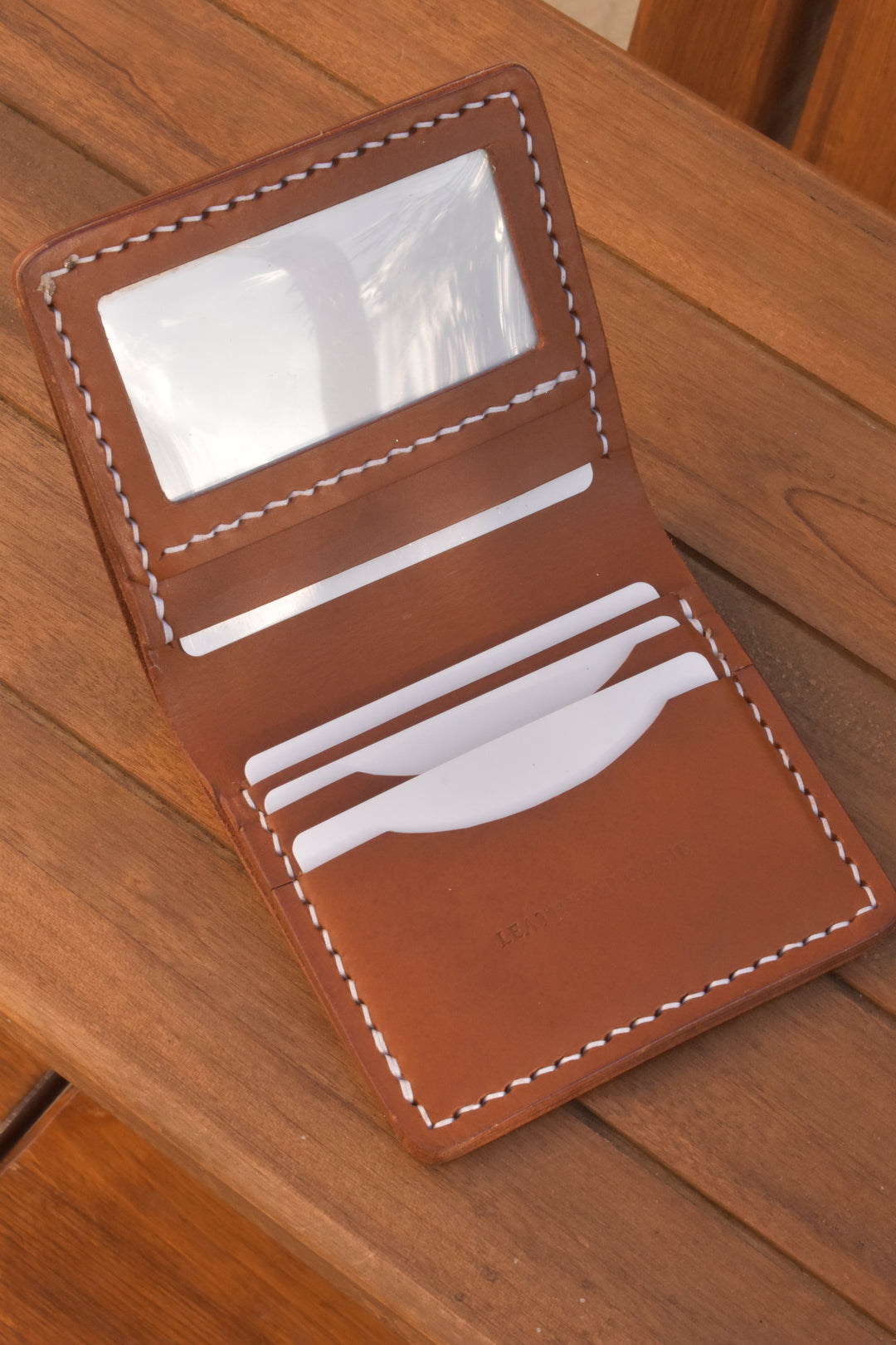 ID bi-fold wallet open view: ID window and card slots, brown leather with white stitching