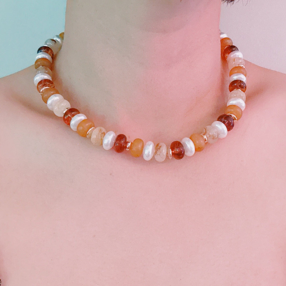 Warm-toned bead necklace on model; orange, amber, and white rounds with gold clasp
