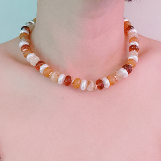 Warm-toned bead necklace on model; orange, amber, and white rounds with gold clasp