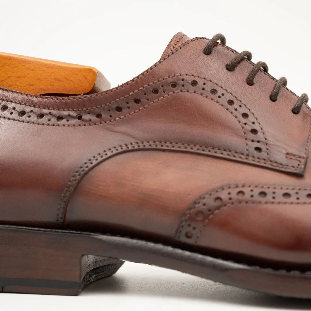 Close-up brown brogue derby shoe, perforated trim along quarter and lace area