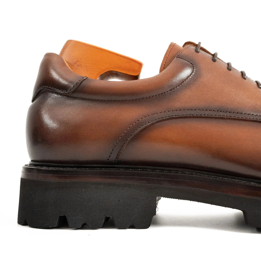 Brown derby shoe side panel detail with lace-up, stitching, and cushioned collar