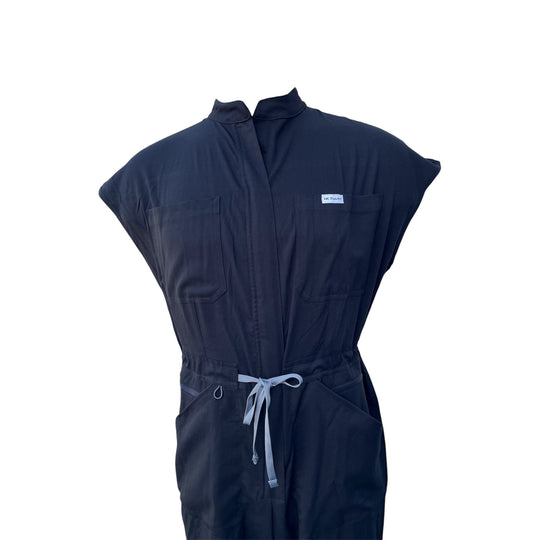 Black scrub jumpsuit detail: front zip placket, patch pockets, drawstring waist ties.