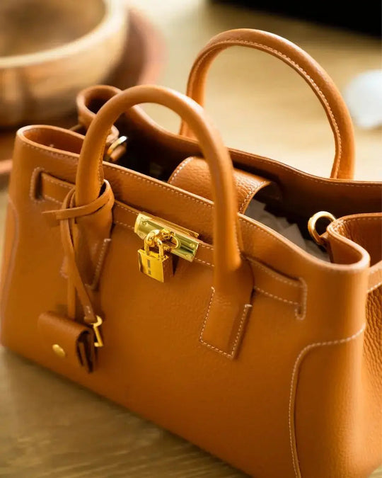 Tan leather satchel close-up with gold lock clasp and stitched trim
