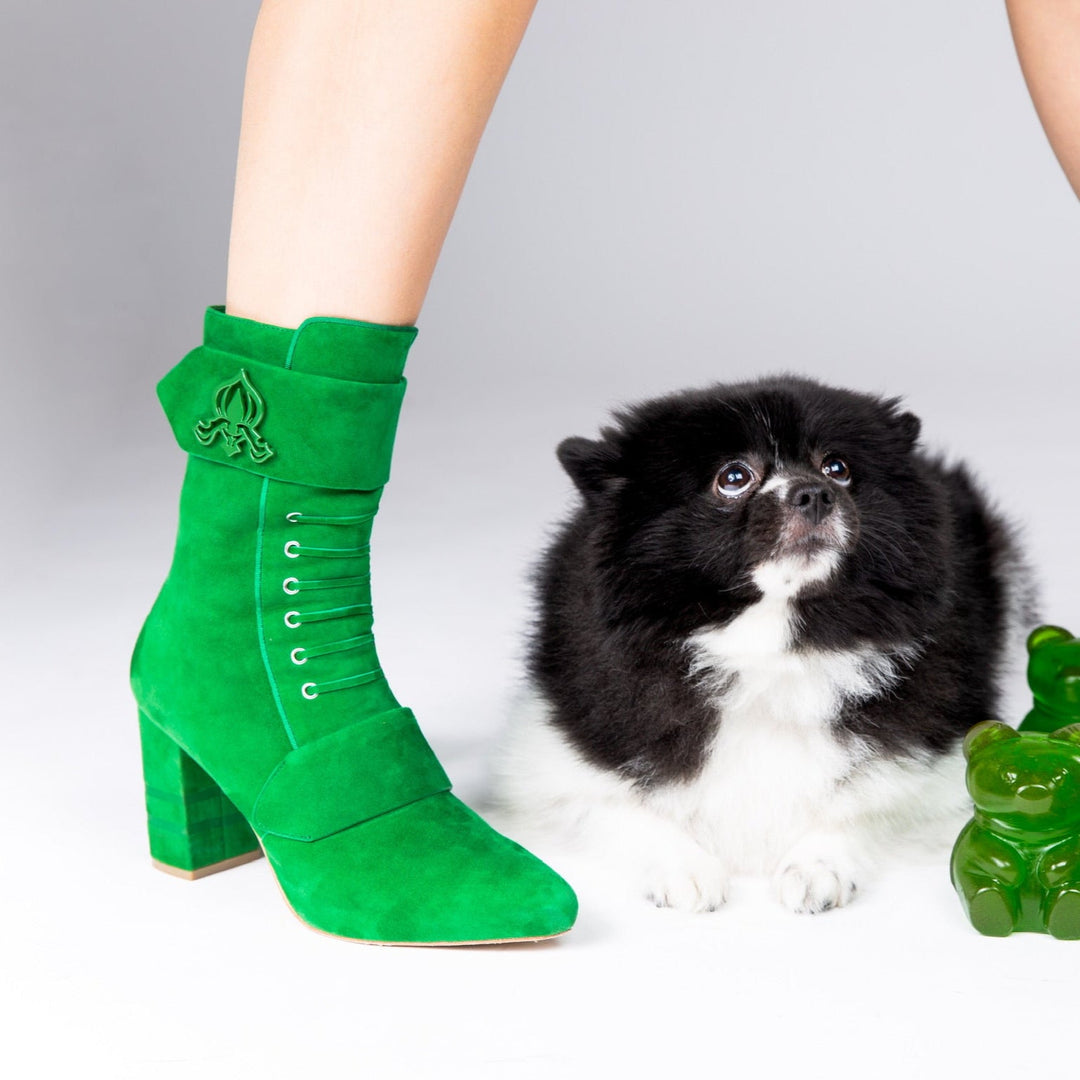 Green suede ankle boots on leg with lace-up eyelets and emblem strap detail