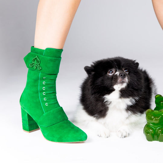 Green suede ankle boots on leg with lace-up eyelets and emblem strap detail