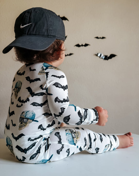 Side view of zippy pajamas on white fabric with black bats and blue skull prints