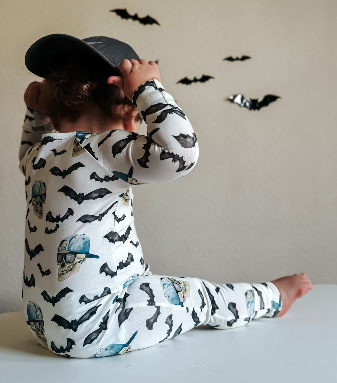Back view of one-piece zippy pajamas with black bat print and blue skulls on white