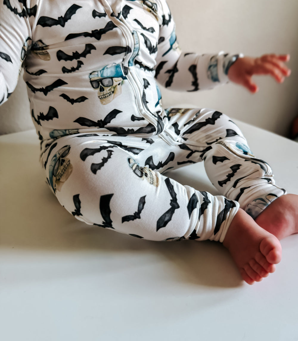 Sleeve and zip details on spooky zippy pajamas; black bats with blue skull graphic on white