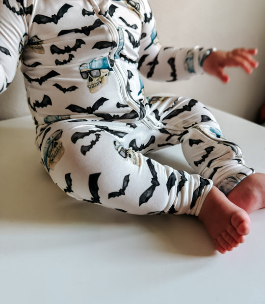 Sleeve and zip details on spooky zippy pajamas; black bats with blue skull graphic on white