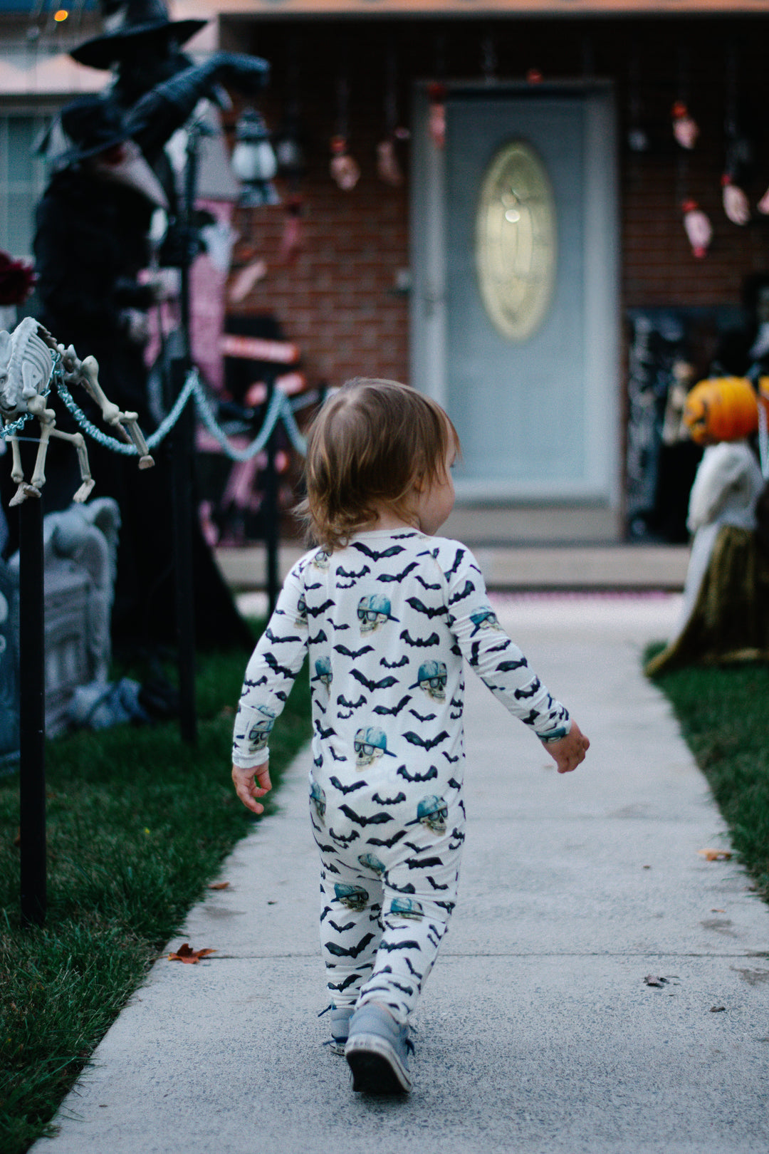 Kid in white spooky zippy pajamas with black bats and blue skull prints, long legs