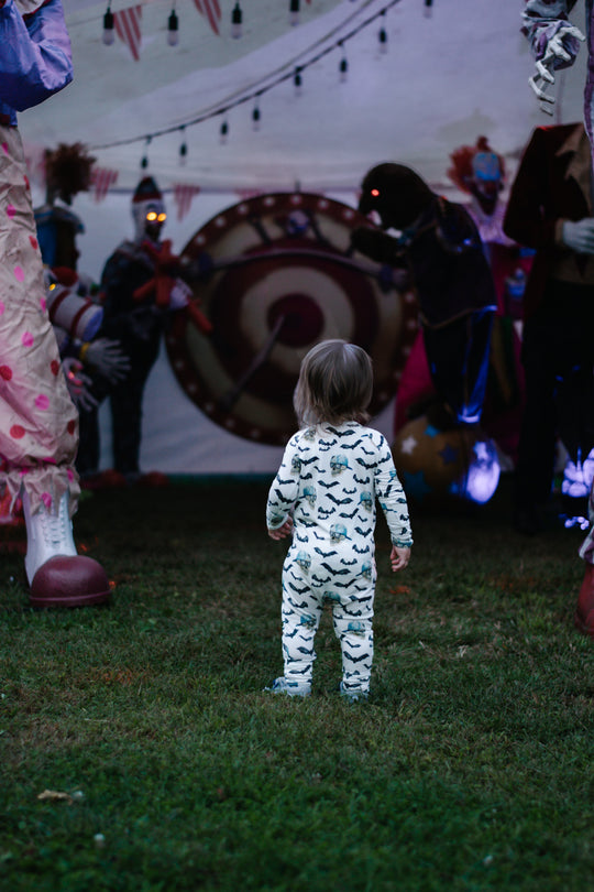 Toddler wearing spooky zippy pajamas in white with black bats and blue skull prints