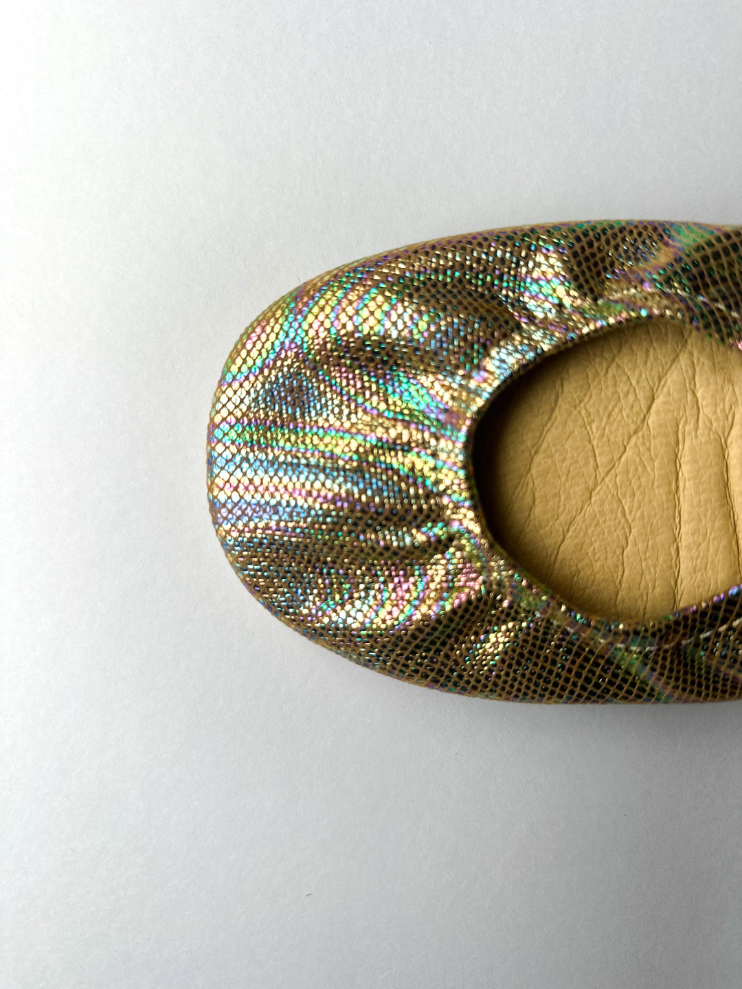 Close-up of metallic iridescent flat toe with cushioned lining and curved opening