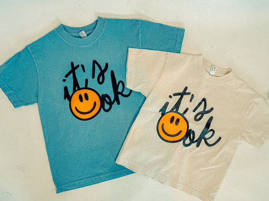 Zwei Kids-T-Shirts: Clear Blue und Ivory, vorne „It’s ok“-Smileyprint
