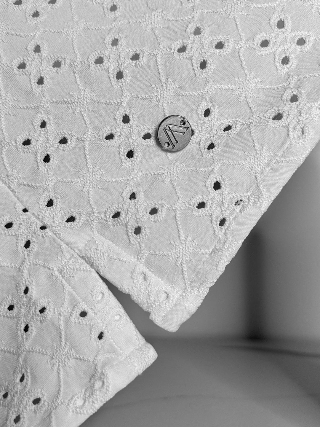 English embroidery texture on off-white fabric, stitched dot pattern and crest