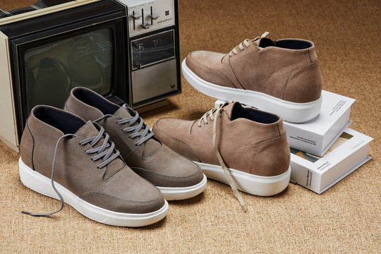 Pair of khaki lace-up boots with white soles and shoelaces, placed near boxes