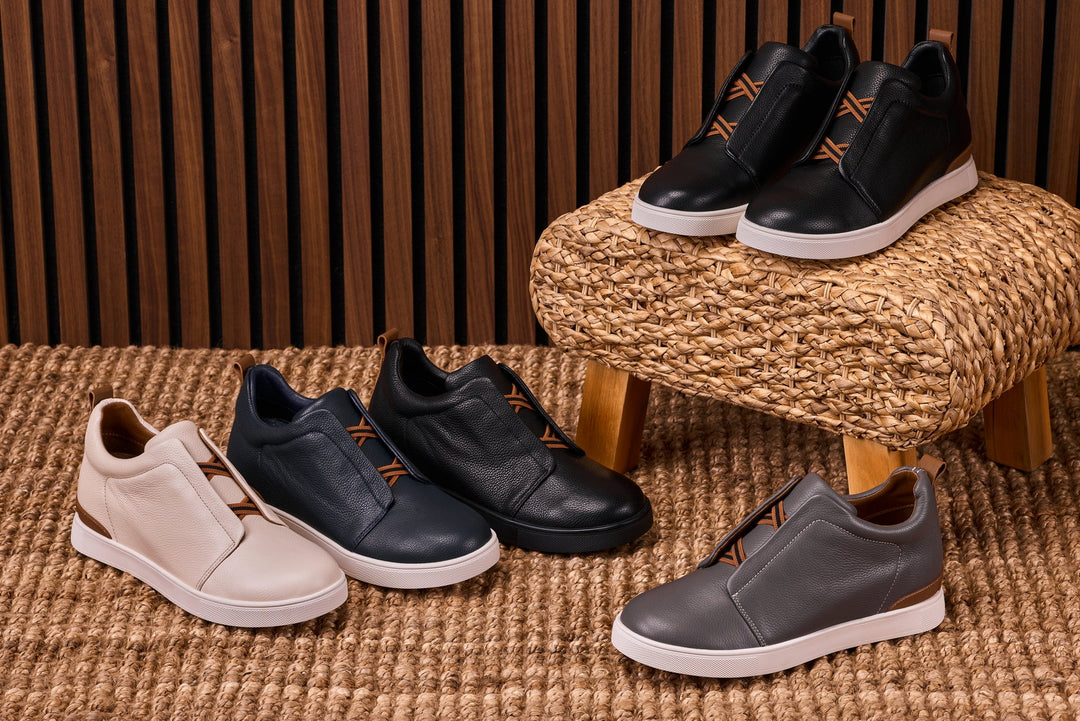 Three slip-on sneakers in white, navy, and gray with orange lace-look accents