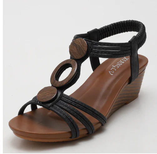 Black Roman-style wedge sandals with crisscross front straps and wood-look ring hardware
