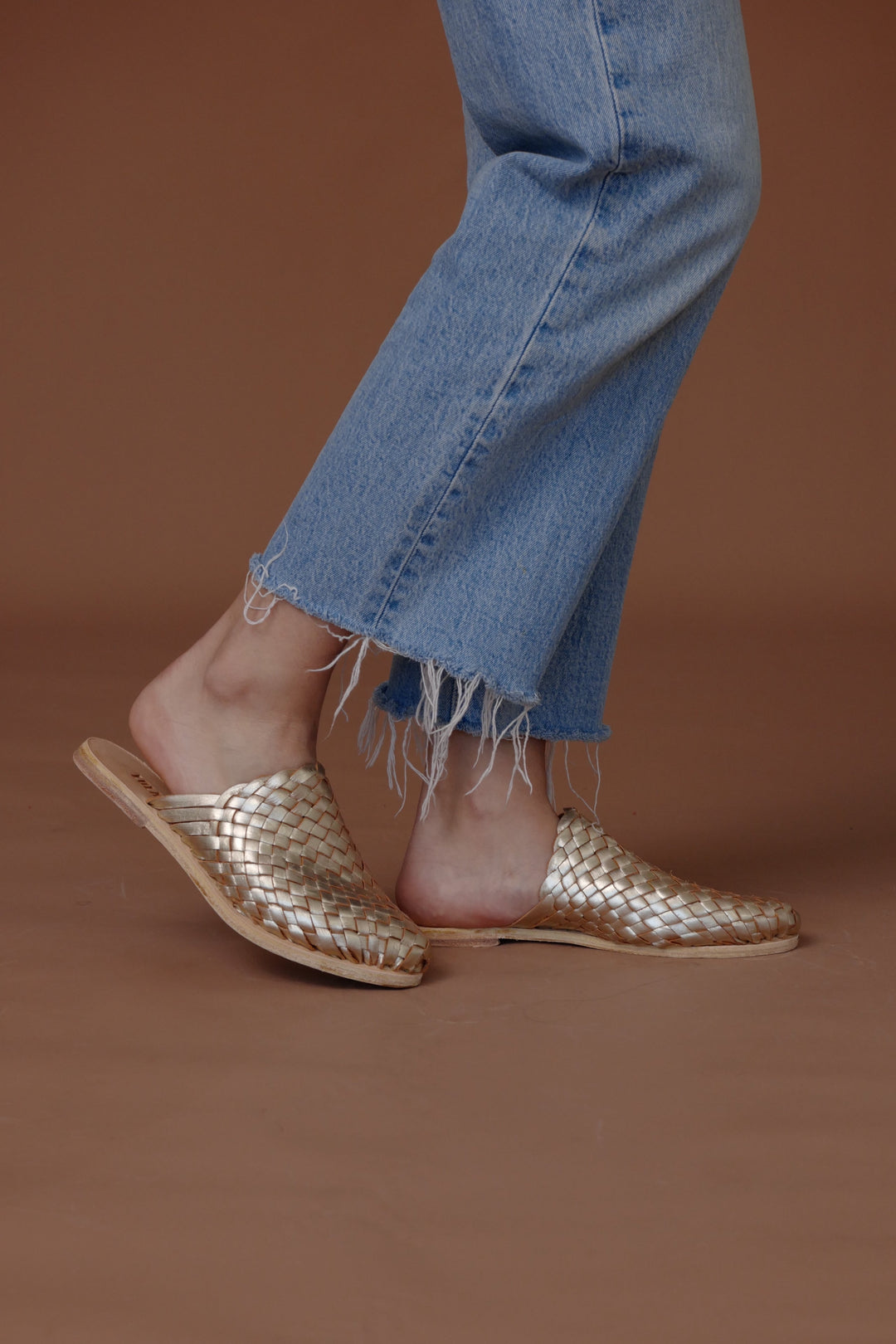 Gold woven leather slide sandals on feet with braided strap upper