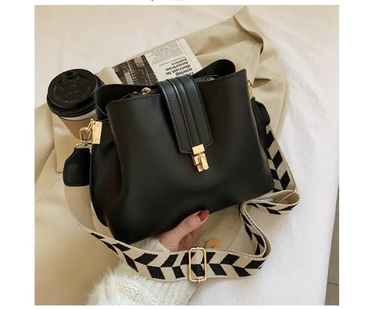 Black bucket bag with patterned crossbody strap and gold-tone front clasp