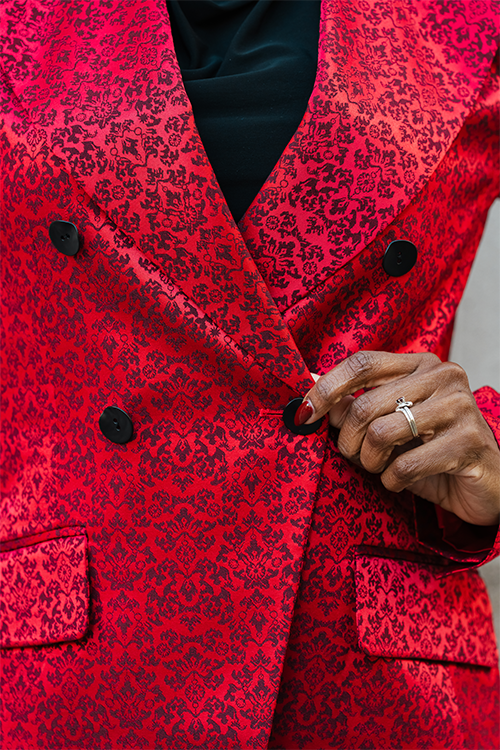 Detailaufnahme: roter Blazerstoff mit Muster, schwarzer Knopf und V-Ausschnitt