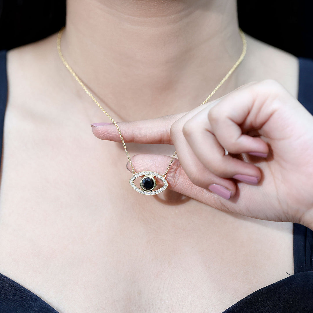 Gold-toned evil eye necklace on hand: oval pendant with dark center stone and pavé trim