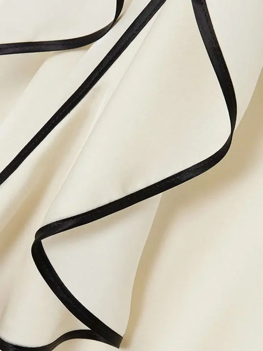 Close-up of white dress fabric with black piping trim along neckline and hem