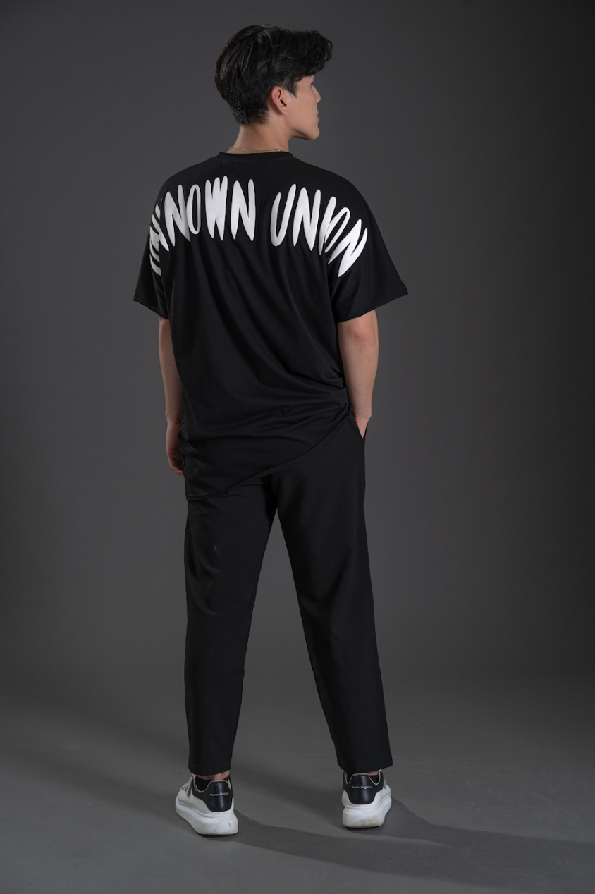 Black T-shirt back view with bold white “UNKNOWN” text graphic across shoulders.