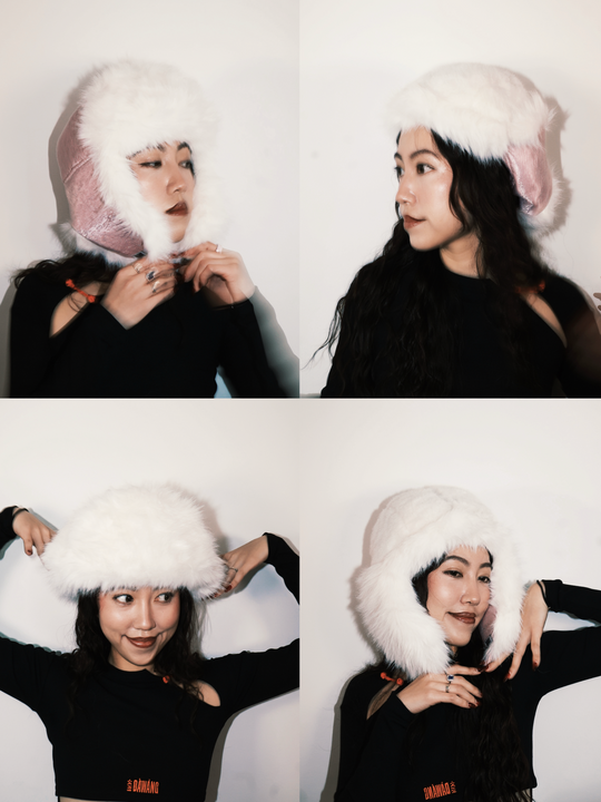 White faux-fur trapper hat worn, with ear flaps and pink tie details