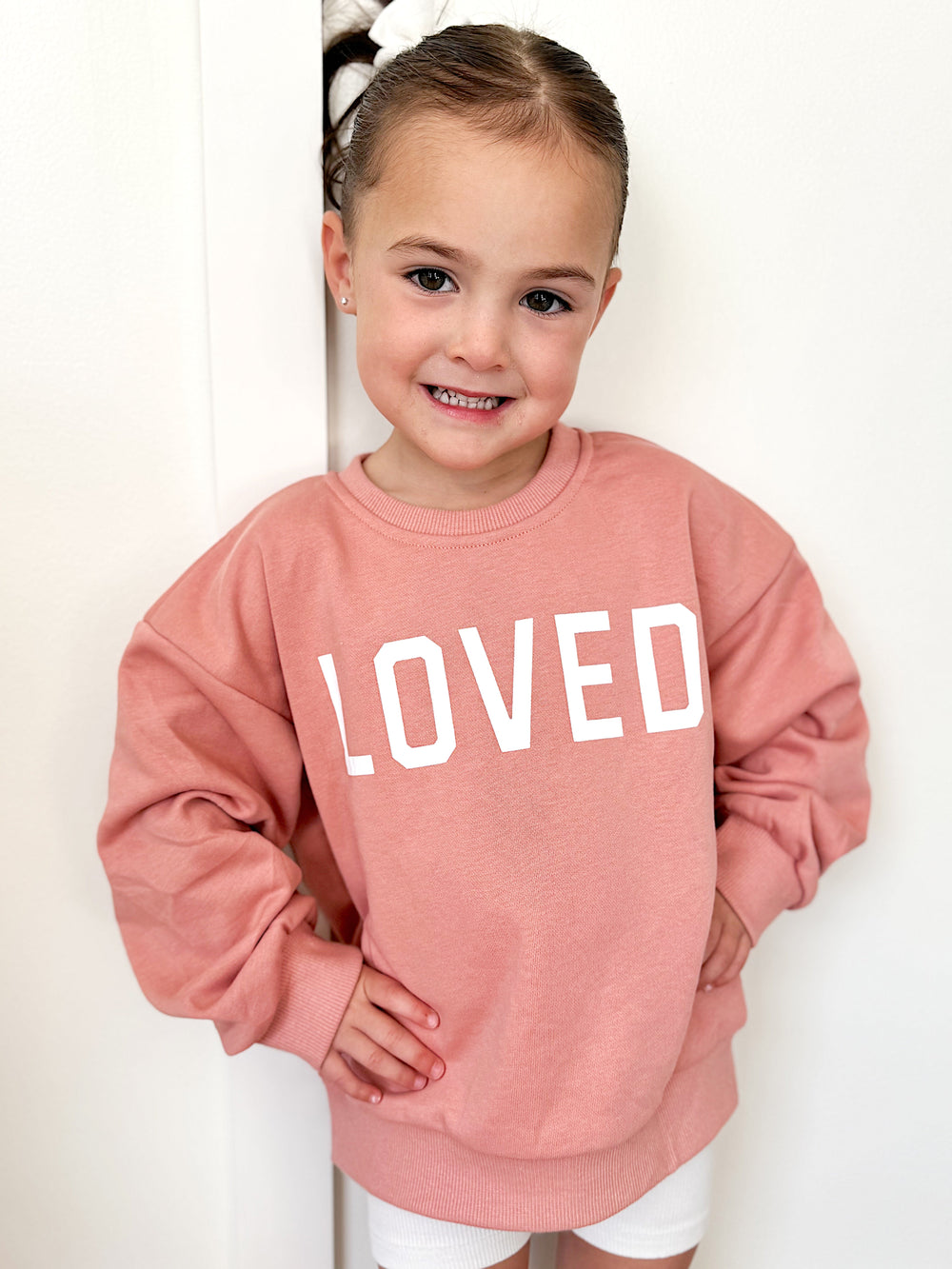 Salmon/pink crewneck sweatshirt with large 'LOVED' text, ribbed collar and cuffs.