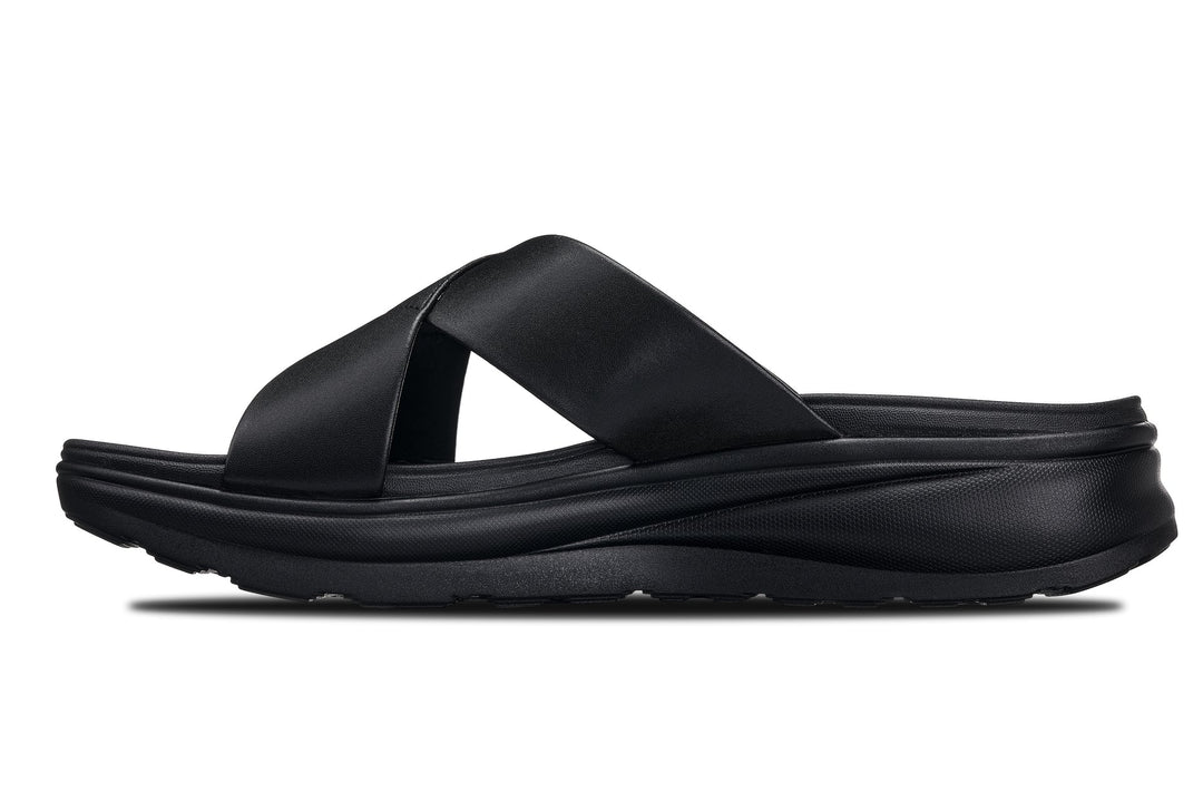 Black matte slide sandals, angled view, wide cross straps over textured platform sole.