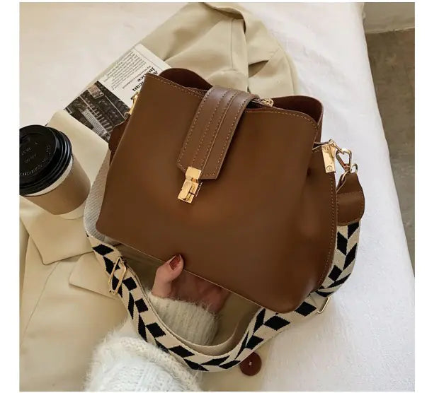 Brown bucket bag with front clasp and crossbody strap, gold hardware details