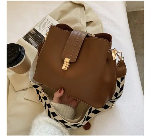 Brown bucket bag with front clasp and crossbody strap, gold hardware details