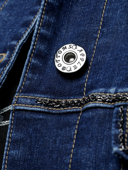 Denim jacket close-up: circular metal snap button on blue denim with chain trim