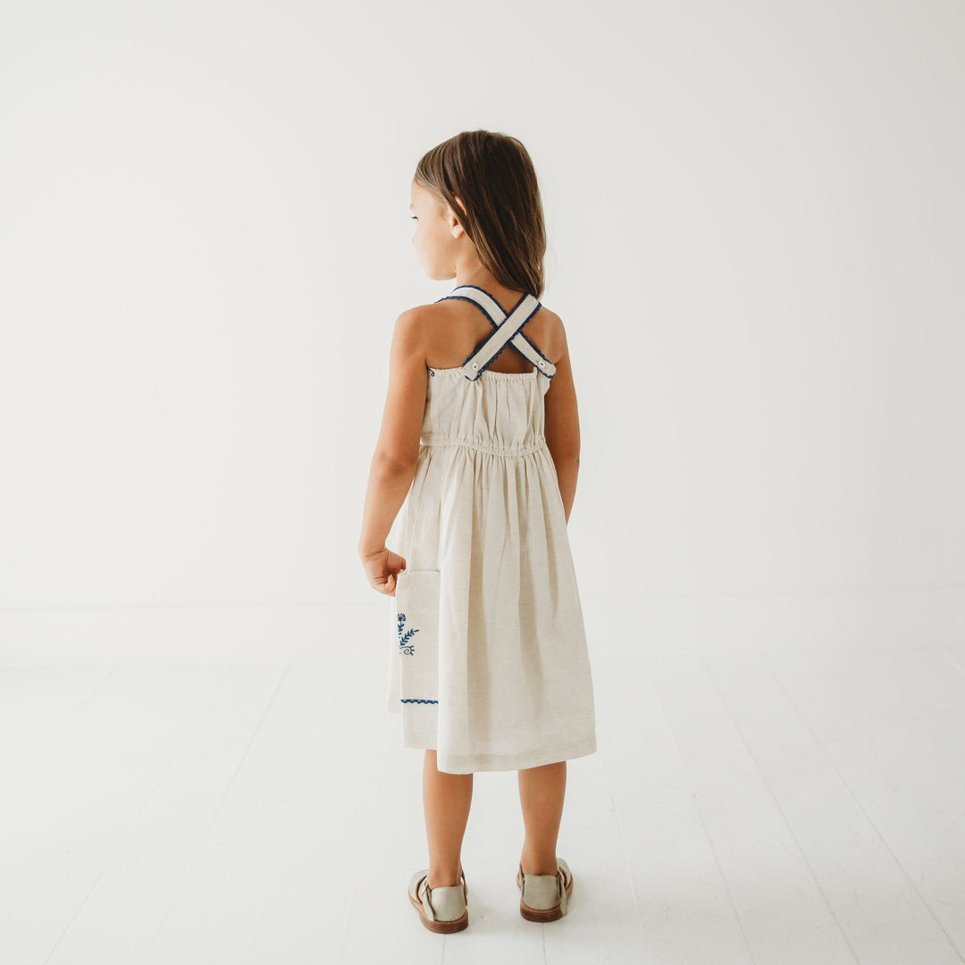 Back view of linen dress with cross-back straps and blue embroidered trim on pockets