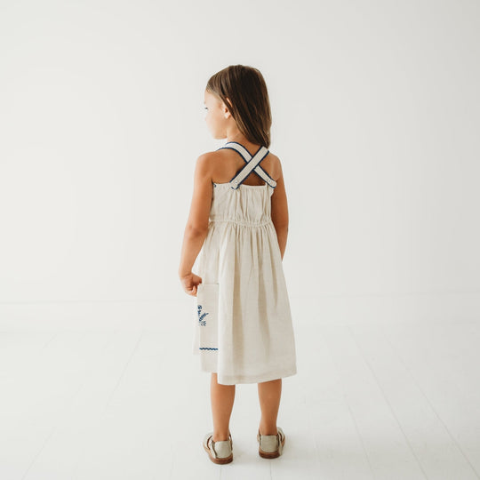 Back view of linen dress with cross-back straps and blue embroidered trim on pockets