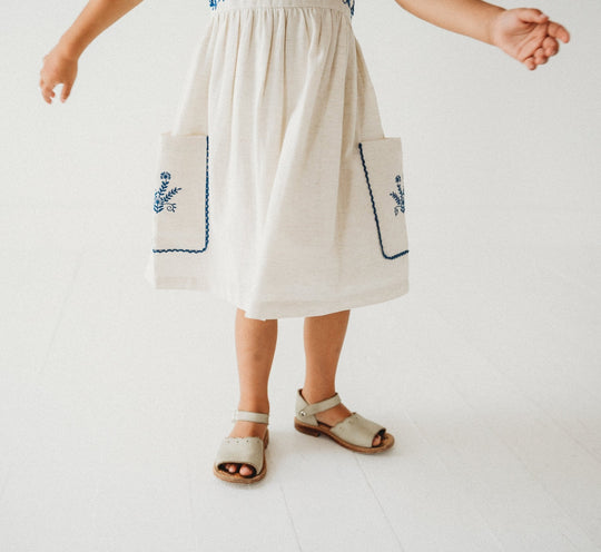Linen dress hem with blue embroidered pocket panels and gathered waistline