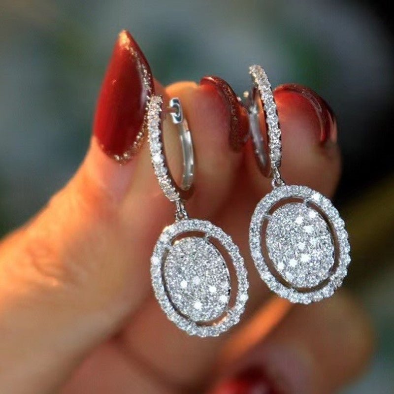 White gold oval dangling earrings with pavé halo and small hoop detail at the ear