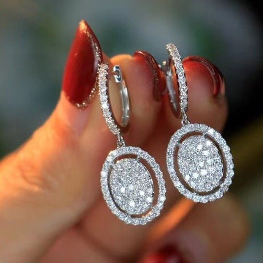 White gold oval dangling earrings with pavé halo and small hoop detail at the ear