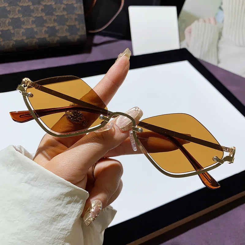 Hand hält Cat-Eye Sonnenbrille mit goldfarbenem Metallrahmen und bernsteinfarbenen Gläsern