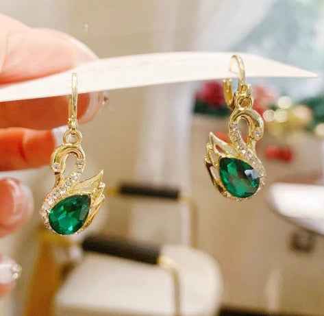 Gold-tone swan earrings with green teardrop center rhinestones and gold hoop.