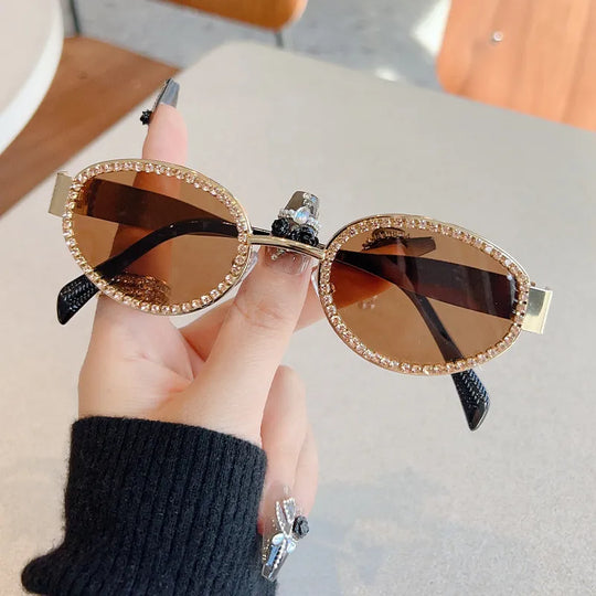 Gold-tone oval sunglasses with rhinestone trim, dark lenses, and jeweled bridge detail