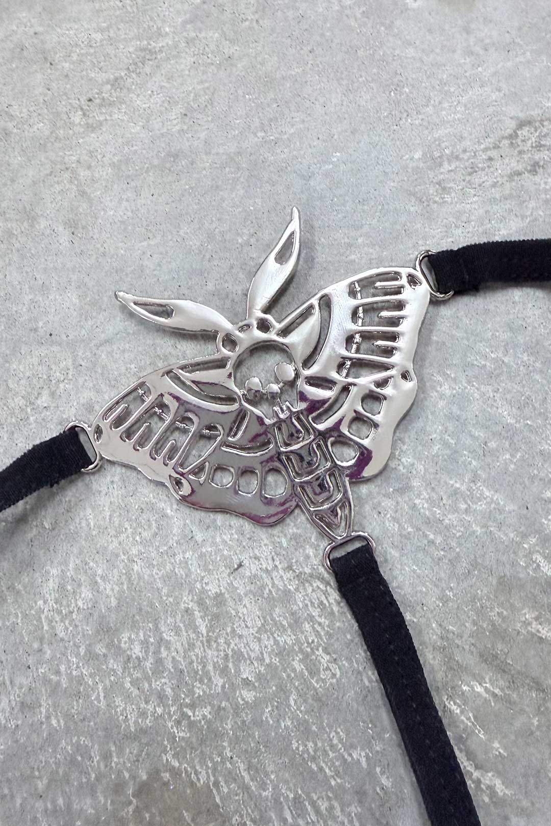 Close-up of silver Death Moth metal charm on black thong straps