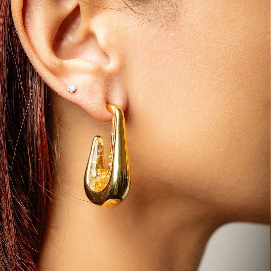 Clear gold leaf drop hoop earrings on ear with gold-tone outer and clear flecked inner