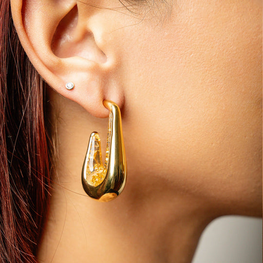 Clear gold leaf drop hoop earrings on ear with gold-tone outer and clear flecked inner