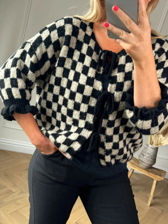 Black-and-cream checkered tie-front knit cardigan with ruffled cuffs and drawstring neckline.