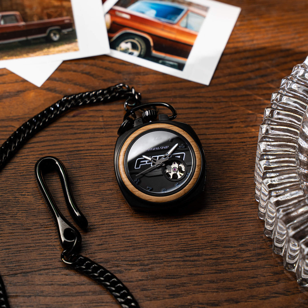 Reloj de bolsillo vintage con cadena negra, caja negra y borde de madera, vista superior.
