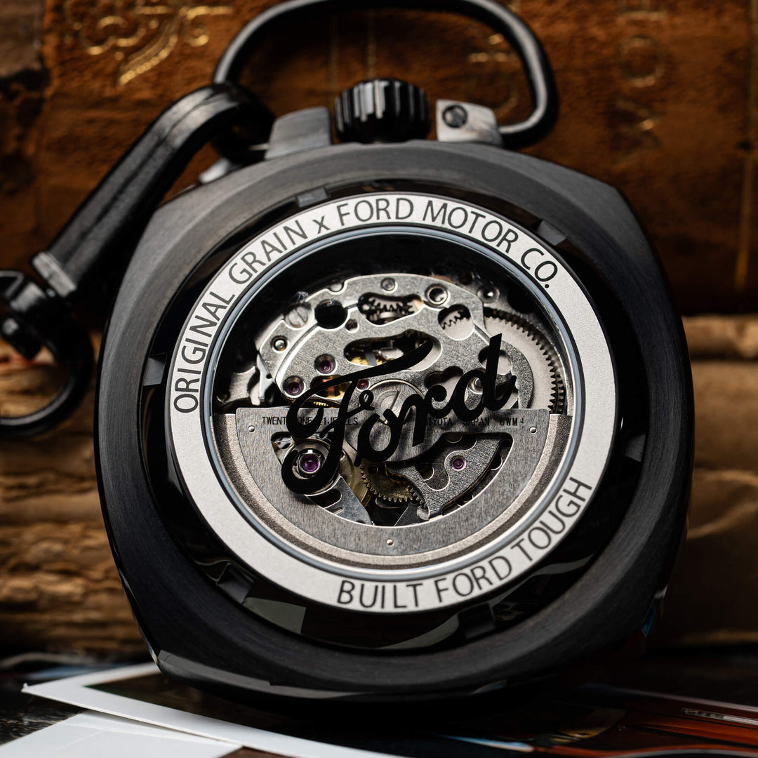 Parte trasera del reloj de bolsillo: mecanismo visible con engranajes y caja negra.