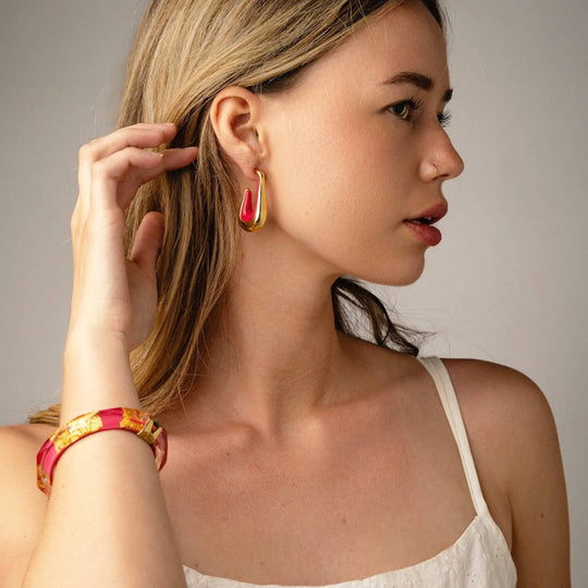 Drop hoop earrings with red-pink enamel inner and gold-tone outer on ear